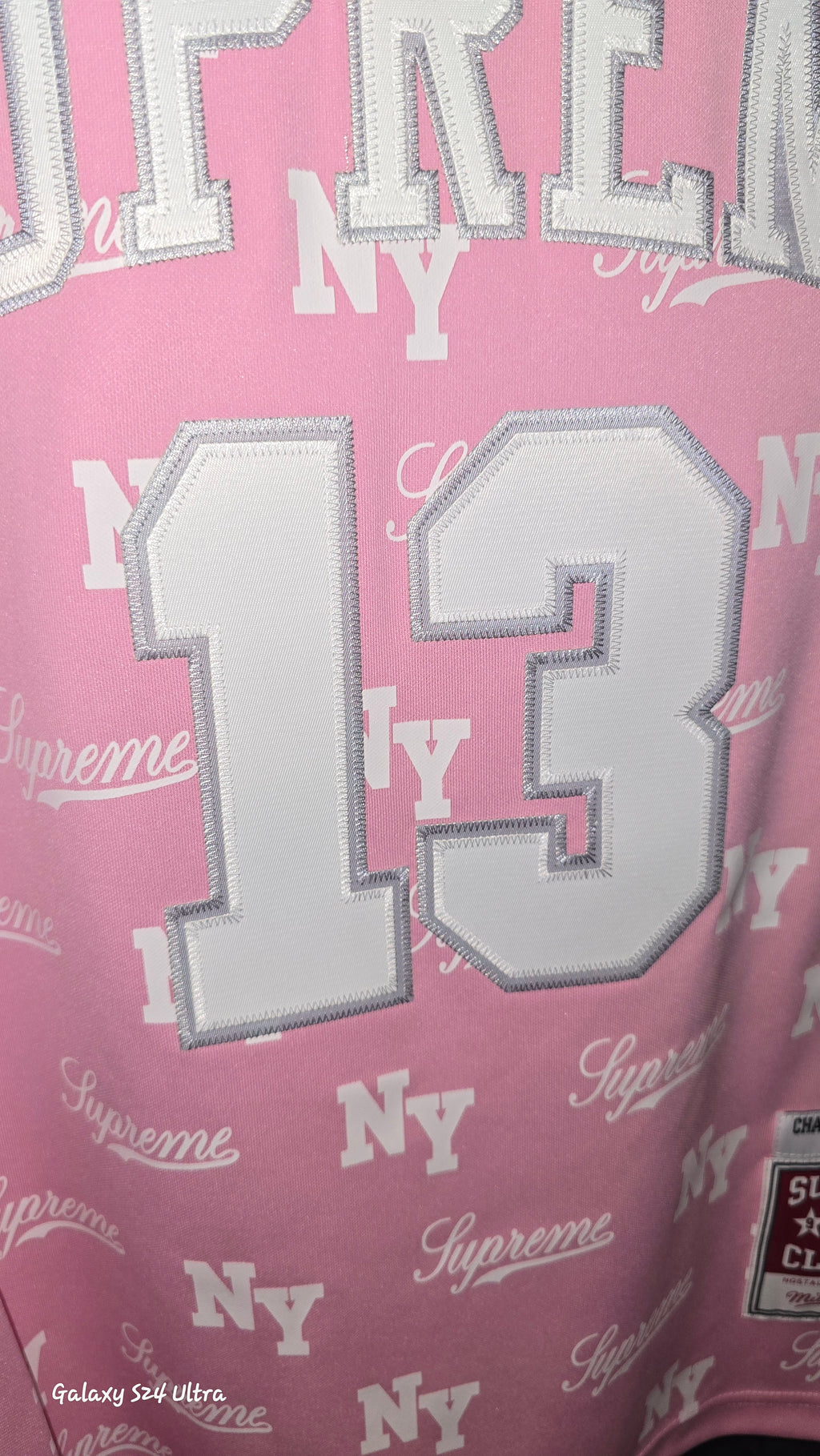 Pink Supreme x Mitchell & Ness monogram basketball jersey features tackle twill appliqué and a matching woven logo label at the lower front.Release Date: May 07, 2026